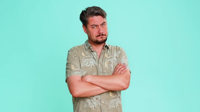 Middle-aged man crosses arms on chest shakes head showing firm position, disapproval or strong disagreement. Young adult guy expresses refusal emotional rejection with body language on blue background