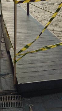 Temporary zone on footpath with hazard. Caution tape surrounds damaged section of pedestrian walkway. Restricted access to walkway with caution tape and uneven metal surface