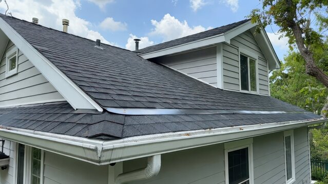Residential home roof and gutter system with asphalt shingles and vinyl siding under sky