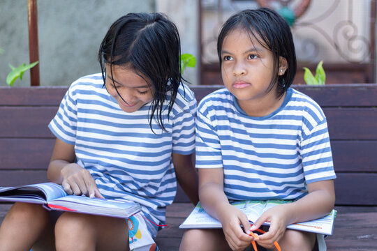 Two girls sitting with books outdoors, one reading while the other looks thoughtful, representing different learning moods and attention in childhood.