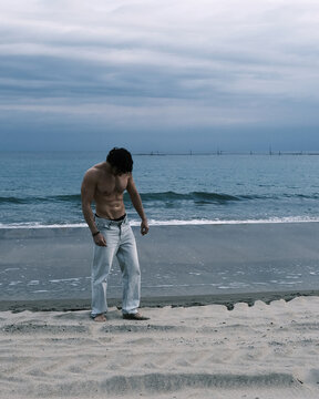 Man with muscular physique standing on a sandy beach by the ocean