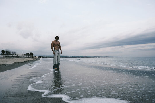 Man standing on a wet beach with waves gently washing over his feet