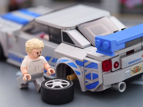 Tambov, Russian Federation - August 21, 2025 Lego Brian OConner minifigure changing wheel of his Lego Speed Champions Nissan Skyline GT-R (R34) car.