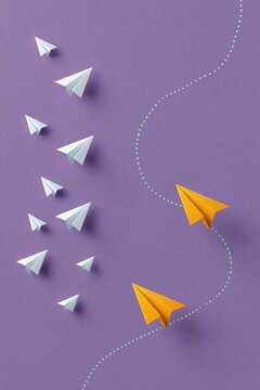 Orange paper planes turning away from formation on purple background