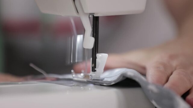 Close-up of a sewing machine needle stitching fabric with a hand guiding the material.