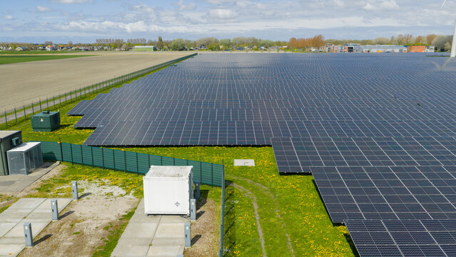 Aerial view of a large solar farm with rows of photovoltaic panels on green grass with yellow wildflowers near the village of Warmenhuizen, North Holland, Netherlands.