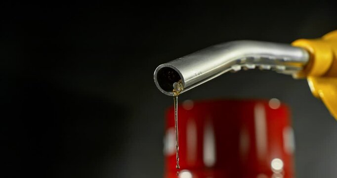 Super slow motion (1000 fps) fuel drops dripping from gasoline nozzle, symbol of depletion and fuel shortage. Minimal liquid flow on black background, dramatic lighting, energy crisis concept.