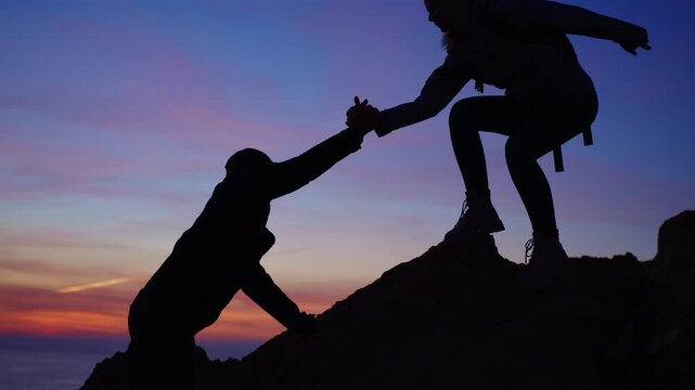 Romantic couple's silhouette against a dramatic sunset,  brave woman extends helping hand to assist partner in climbing down steep mountain, symbolizing support and teamwork