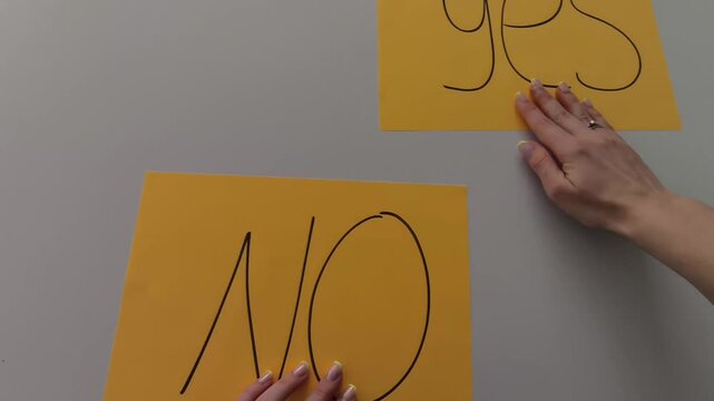 Close-up of a woman&rsquo;s hands sliding two paper cards labeled &ldquo;Yes&rdquo; and &ldquo;No&rdquo; across a table, finally leaving &ldquo;Yes&rdquo; in place. Minimal, clean visual illustrating decision-making, choice, and positive outc