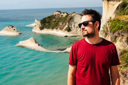 Smiling man standing by Turquoise sea cliffs in Corfu, Greece