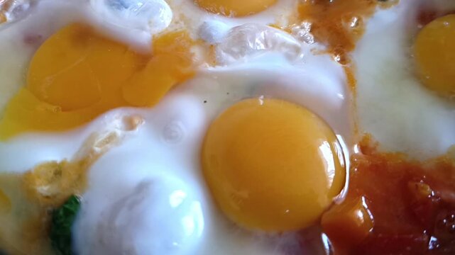 A pan in which the dish "shakshuka" is being cooked (eggs simmered in a sauce of tomatoes, peppers, and spices), close-up