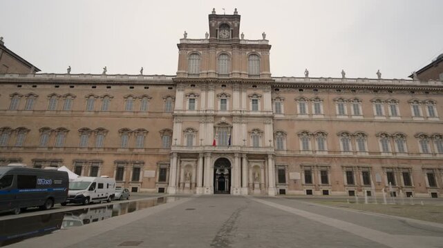 Modena, italy, april 12, 2026. Pov shot walking towards the historic facade of the ducal palace in modena, italy. Majestic baroque architecture on a cloudy day