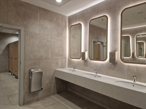 Modern public restroom with backlit mirrors, stone tiles, and white integrated vanity sinks