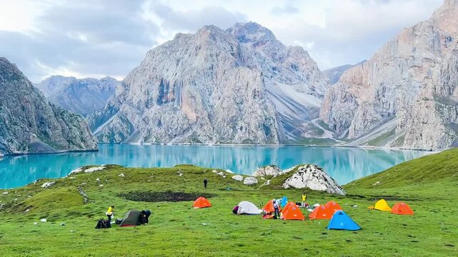Xinjiang, China - 27 July 2024: Many tents are set up on the grassy hills by the clear blue waters of Tientang Hu lake, Xinjiang, China. There are many mountains reflected in the water. 