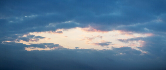 Obraz premium Dramatic twilight sky with a gap between clouds where warm pink-golden hues contrast with deep blue — atmospheric sunset