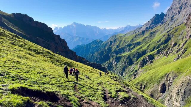 Wide-angle video of green grassy hills on both sides at Tianshan Mountain, Xinjiang, China. Hikers are walking in the distance on a sunny day. Idea for adventure footage with copy space.