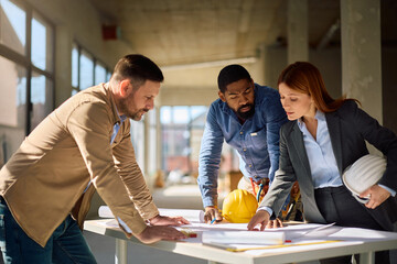 Black worker and real estate developers going through plans at construction site. © Drazen
