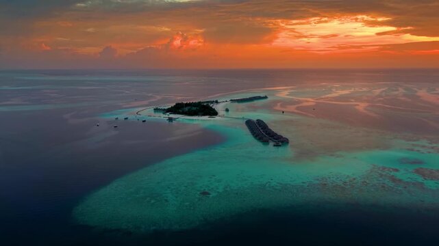 A beautiful paradise island in the Maldives with water bungalows over the turquoise ocean with shining coral reefs during a dramatic sunset