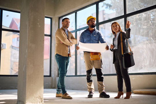 Black construction worker and building contractors talking while analyzing blueprints on site.