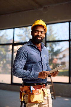 Happy black construction site foreman using digital tablet and looking at camera.