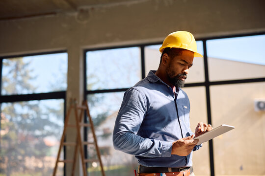Black construction worker going through plans on digital tablet.