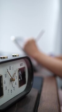 Close-up of a vintage alarm clock with ticking second hand and blurred background of a person using a digital tablet and stylus, time management and productivity concept