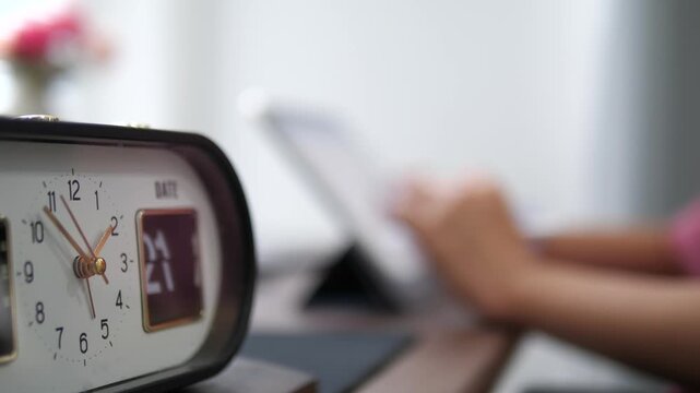 Close-up of a vintage alarm clock with ticking second hand and blurred background of a person using a digital tablet and stylus, time management and productivity concept