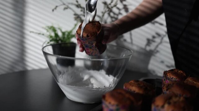 Woman spreading white icing on easter cake with spoon in kitchen close baking process traditional festive dessert preparation