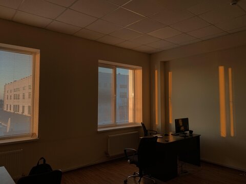 Sunlight streams through windows casting shadows in a quiet modern office with empty desks and chairs.
