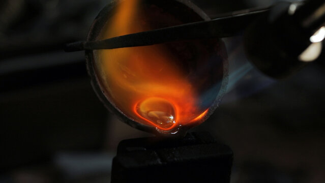 Molten gold glowing in a crucible under intense heat, captured in a close-up with vibrant orange and yellow hues.