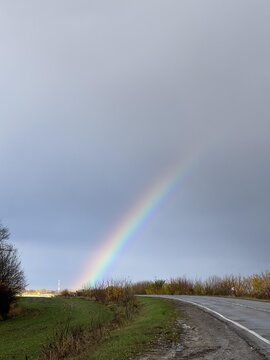 A vibrant rainbow arches over a serene landscape, illuminating a tranquil rural scene after rainfall.