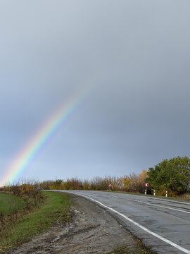 A beautiful rainbow arcs over a tranquil road, framed by autumn foliage and a calm sky.