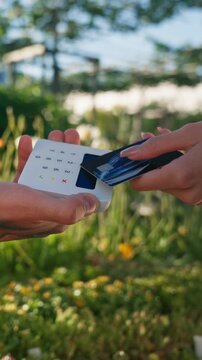 Portable Payment Device. Customer Makes Payment With Small Device Amid Blooming Flora And Trees