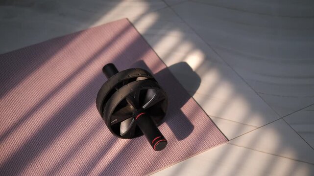 Cinematic close-up of an ab roller wheel on a pink yoga mat with beautiful window blind shadows, home workout and core fitness concept