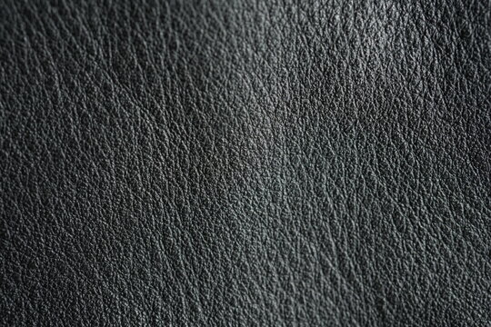 macro texture of black biker leather jacket viewed from top. Close-up of genuine or synthetic leather surface showing natural grain, subtle wrinkles, and matte to slightly glossy finish. Minimal and s