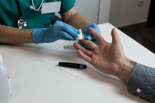 A medical professional cleaning a patient's fingertip with an alcohol swab to ensure a sterile procedure for glucose level testing.