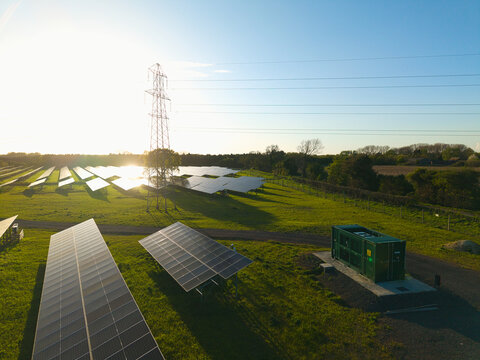 Aerial view of Tiln Photovoltaic Solar Farm and Battery Energy Storage System with rows of solar panels, an electricity pylon, and green fields under a bright sun Retford, England, United Kingdom.