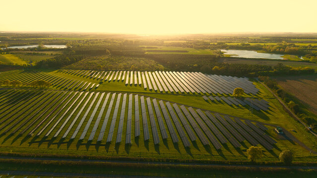 Aerial view of Tiln Photovoltaic Solar Farm and Battery Energy Storage System with rows of solar panels across green fields at golden hour in Retford, England, United Kingdom.