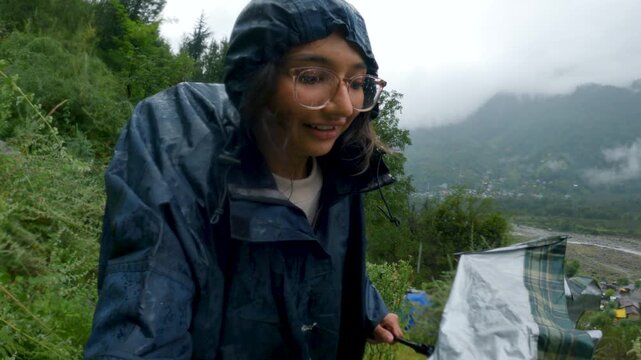4K Selfie shot of Indian woman hiking in rain. Hiker hiking in mountains during monsoon season at Manali, Himachal Pradesh, India. Outdoors adventure trek activity, wearing waterproof raincoat. 
