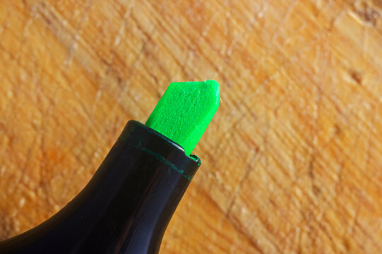 Close-up of a bright green highlighter pen tip against a textured wooden background