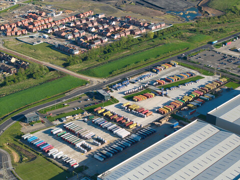 Aerial view of Iport Avenue featuring rows of colorful shipping containers and trucks parked at a logistics hub near a residential neighborhood in Loversall, England, United Kingdom.