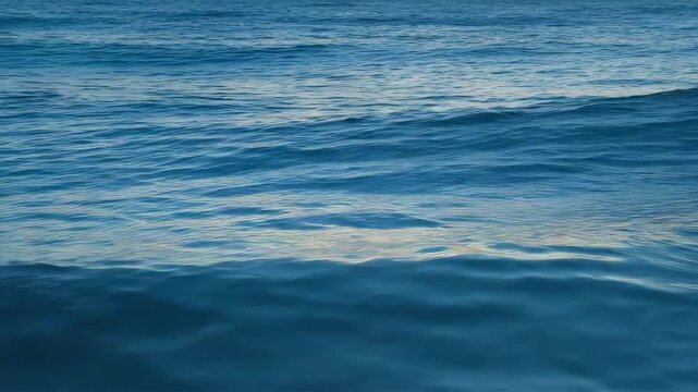 Aerial ocean waves, deep blue water surface, gentle rolling swells, serene sea texture, cinematic ocean motion