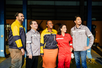 Fototapeta premium Diverse team of industrial workers in protective workwear stand together in a workshop, smiling and looking ahead, suggesting teamwork, maintenance, and engineering in a garage environment.