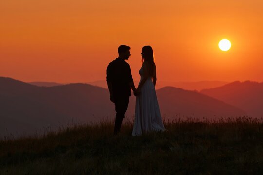 Couple Holds Hands During Sunset on a Hilltop With Mountains in the Background