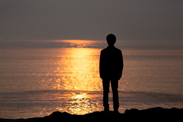 Fototapeta premium Silhouette of Businessman Standing by the Sea at Sunset Reflecting on
