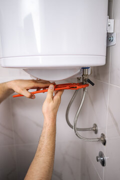 Plumber working on water heater using adjustable wrench in bathroom