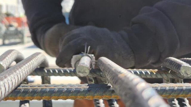 Slow motion front view of a worker tying steel rebar on a scaffold with focus on the hands and material.