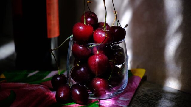 Plump and juicy cherries glisten in the glass, their deep red skins hinting at perfect ripeness. The room is bathed in the gentle light of early morning, while the lingering twilight casts soft shadow