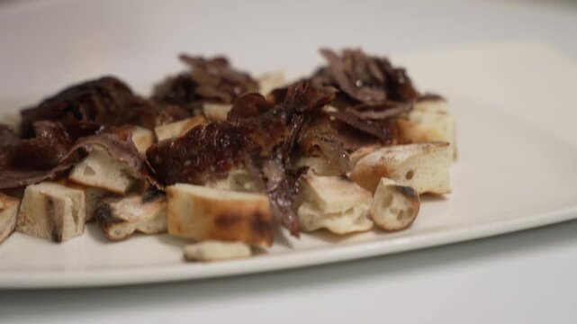Professional chef arranging sliced doner meat over pide bread for an Iskender Kebab on a white plate, fa01