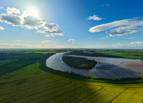 Aerial view of Howden Dyke Island in the River Ouse surrounded by vibrant yellow rapeseed fields and green meadows under a bright sunny sky Goole, England, United Kingdom.